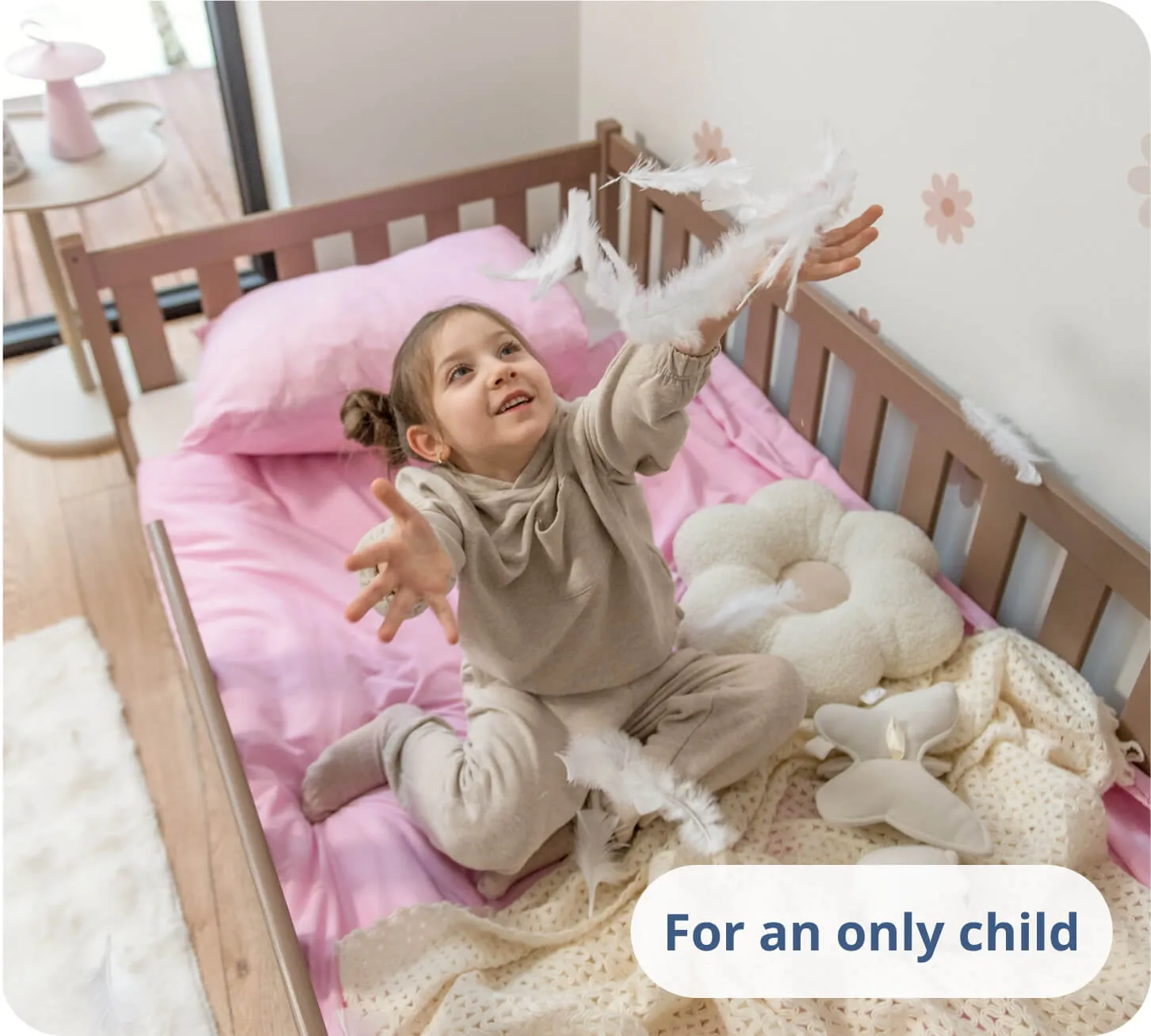 Young girl playing with white feathers on pink bedding in a chocolate-colored bed.